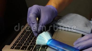 一个戴着橡胶手套的人<strong>用</strong>棉签在键盘之间清洁笔记本<strong>电脑</strong>键盘。 笔记本<strong>电脑</strong>的清洁和维护。